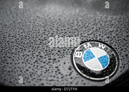 BMW badge Raindrops Munich Allemagne // MUNICH, Allemagne — vue rapprochée d'un badge BMW sur le capot d'une voiture BMW noire, couvert de gouttes d'eau de pluie. La faible profondeur de champ souligne le logo bleu et blanc emblématique du célèbre constructeur allemand de luxe, soulignant la précision et la qualité associées à la marque. Banque D'Images
