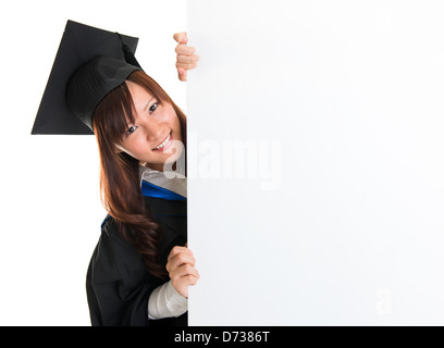 Portrait of smiling Asian female student en robe d'études supérieures d'oeil, de se cacher derrière une carte blanche, isolé sur fond blanc Banque D'Images