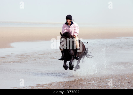 Une jeune femme équitation poney son animal de compagnie sur la plage, Holkham Beach Norfolk, UK Banque D'Images