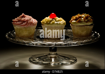 Studio shot of three Cupcakes cake stand sur le verre, sur un fond noir. Banque D'Images