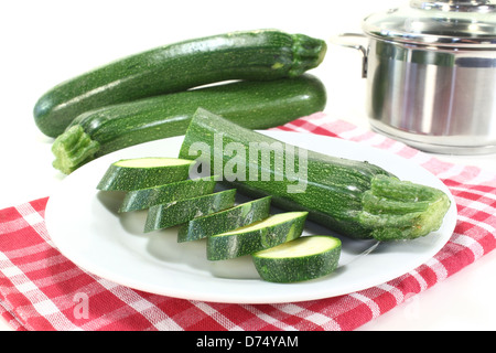 Courgette en tranches fraîches sur une plaque avec pot en face de fond clair Banque D'Images