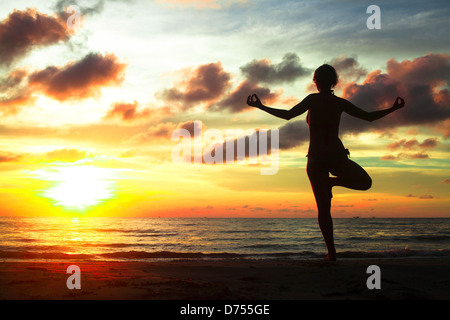 Young woman practicing yoga sur la plage au coucher du soleil.
