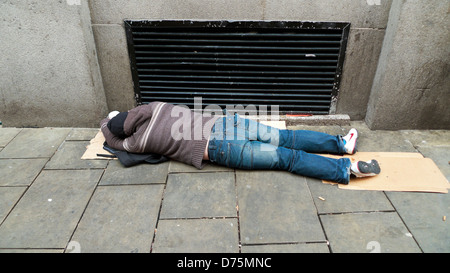 L'homme endormi se prosterner (peut-être ivre ou gueule) passés sur la chaussée par l'évent de chauffage pour garder au chaud Swansea Pays de Galles UK KATHY DEWITT Banque D'Images