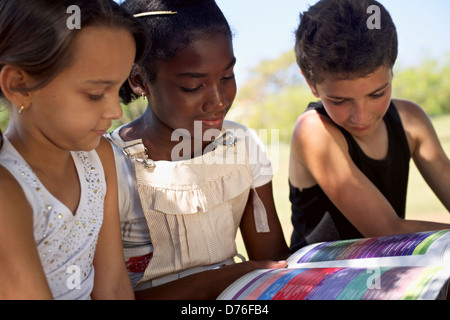 Les jeunes et l'éducation, deux petites filles et un garçon reading book in city park Banque D'Images
