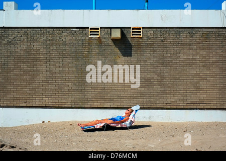 Une femme se trouve dormant sur un transat sur la plage de Coney Island, Brooklyn, New York. Banque D'Images