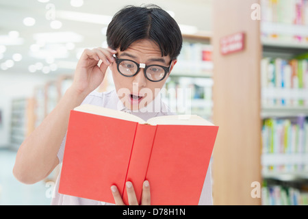 Nerdy homme voit quelque chose d'étonnant dans un livre Banque D'Images