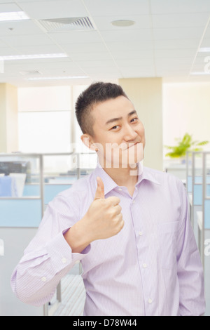 Young man giving Thumbs up sign in office, portrait Banque D'Images