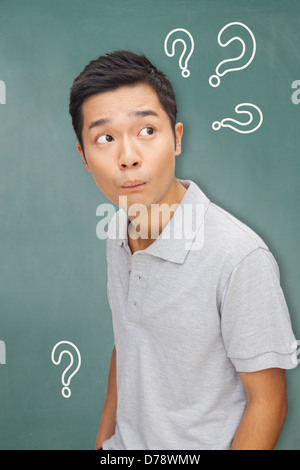 Portrait young man in front of blackboard with question marks Banque D'Images