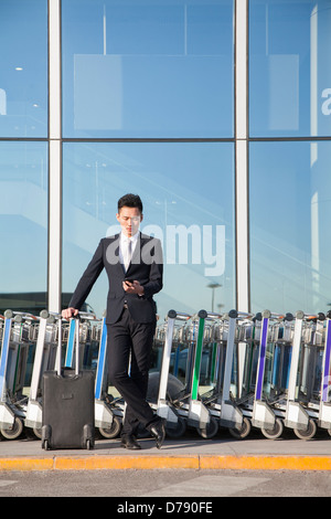 Meilleur à la téléphonie cellulaire à côté de rangée de chariots à bagages Banque D'Images