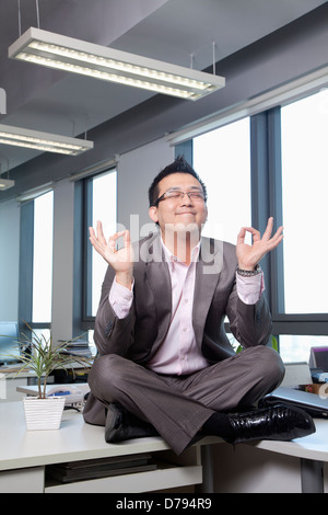 Businessman sitting on desk in office de la méditer Banque D'Images
