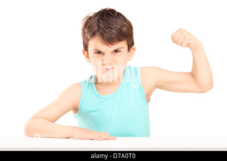 Un enfant fou montrant ses muscles assis sur une table isolé sur fond blanc Banque D'Images