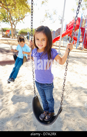 Boy and Girl Playing On Swing In Park Banque D'Images