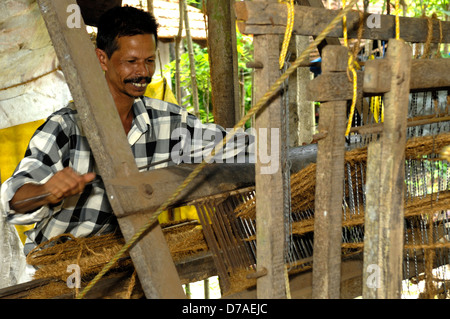 L'homme à l'aide de fibres de noix de coco twin sur métier à tisser en bois produisant des paillassons en coco home cottage-industrie, Kerala, Inde Banque D'Images