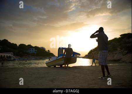 Après une journée au soleil un pédalo est tiré hors de l'eau comme le soleil se couche sur Portinatx, Ibiza. Banque D'Images