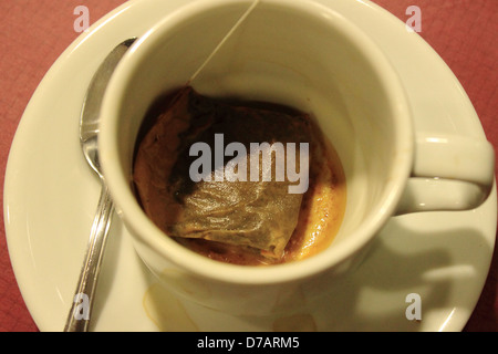 Un sachet de thé utilisé à l'intérieur d'une tasse sur une soucoupe volante. Une cuillère est également mis sur la soucoupe. Banque D'Images