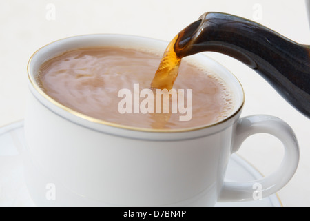 Faire verser une tasse de thé anglais traditionnel d'un bec de théière dans une tasse de thé en porcelaine blanche avec du lait mis en premier. Angleterre Royaume-Uni Grande-Bretagne Banque D'Images