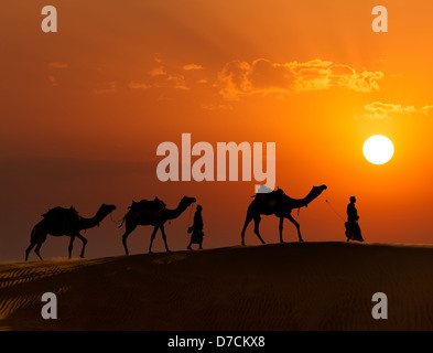 Arrière-plan de voyage Rajasthan - deux chameliers indiennes (chameliers) avec des chameaux silhouettes dans les dunes du désert de Thar au coucher du soleil Banque D'Images