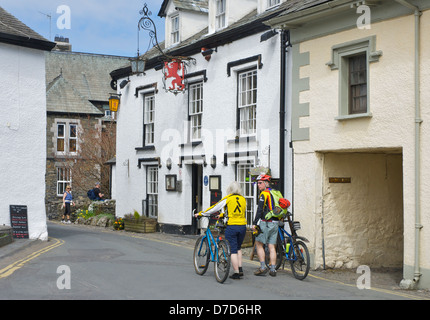 Deux cyclistes en passant devant le Red Lion Inn, à Hawkshead, Parc National de Lake District, Cumbria, Angleterre, Royaume-Uni Banque D'Images