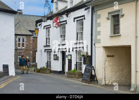 Young Asian couple walking passé le Red Lion Inn, à Hawkshead, Parc National de Lake District, Cumbria, Angleterre, Royaume-Uni Banque D'Images