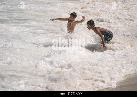 Deux garçons s'amuser avec les vagues à la plage de Leme, sur une journée ensoleillée d'automne. Rio de Janeiro, Brésil Banque D'Images