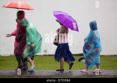 Bangkok, Thaïlande. 5 mai, 2013. Les touristes avec umbellas à pied à travers un orage passé les parois du Grand Palais avant l'Bhumibol Adulyadej, le Roi de Thaïlande, arrivé pour un événement de jour du couronnement. Le 5 mai marque le 63e anniversaire du couronnement de Sa Majesté le Roi Bhumibol Adulyadej. La journée est célébrée comme une fête nationale ; depuis cette année, il tombe un dimanche, le jour férié sera célébrée le lundi 6 mai, et à ce titre tous les bureaux gouvernementaux et les banques commerciales se ferme pour la journée. Sa Majesté le Roi Bhumibol Adulyadej est le plus ancien monarque régnant dans le monde. Chaque année le Banque D'Images