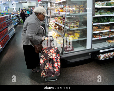 Vieille femme noire shopping shopping pour la nourriture regardant l'affichage de fruits avec un chariot de sac à provisions Marks & Spencer magasin Cardiff pays de Galles UK KATHY DEWITT Banque D'Images