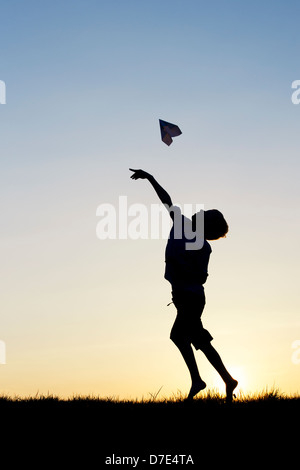 Garçon en train de lancer un avion en papier au coucher du soleil. Silhouette Banque D'Images