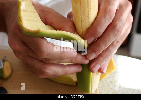 L'homme les mains soigneusement éplucher la peau épaisse de fruits plantain à prêt pour la friture à l'huile vierge et des assaisonnements. Banque D'Images