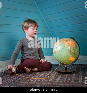 Un jeune enfant regarde un illuminé globe penser à des endroits éloignés assis dans un confortable chambre mansardée à la lumière Banque D'Images