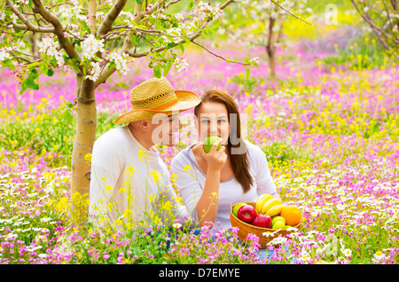 Young happy family having picnic sur champ de fleurs au printemps, le jardin de manger sain Aliments biologiques, maison de vacances et de vacances Banque D'Images