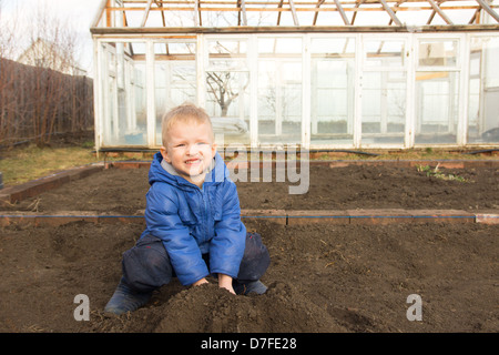 Happy smiling joyeuse enfant (garçon) de creuser le sol, travaillant dans la région de Spring Garden Village. Peu d'agriculteurs. Banque D'Images