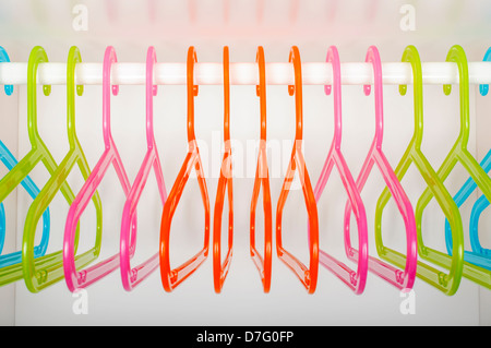Cintres en plastique colorés accrochés sur une tige dans une penderie blanche vide Banque D'Images