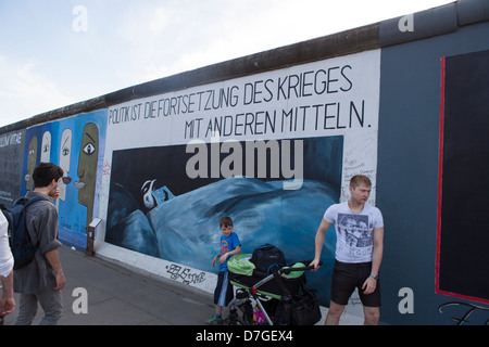 Père et fils passant d'un tableau sur le mur de Berlin avec le texte : La paix se passe de la guerre avec d'autres services publics. Banque D'Images