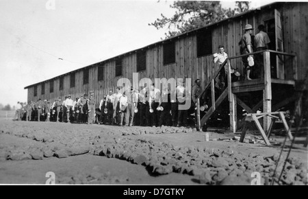 Cette photographie montre des membres du Civilian conservation corps (CCC) alignés à l'extérieur d'une caserne dans un camp. L'image, qui fait partie de la collection Gerald W. Williams, offre un aperçu de la vie dans un camp de CCC pendant la Grande dépression, mettant en valeur le programme de secours au travail. Banque D'Images