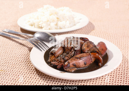 Assiette de petits calmars sautés mijotée dans la sauce soja et de vinaigre, avec une fourchette, une cuillère et le riz en arrière-plan. Banque D'Images