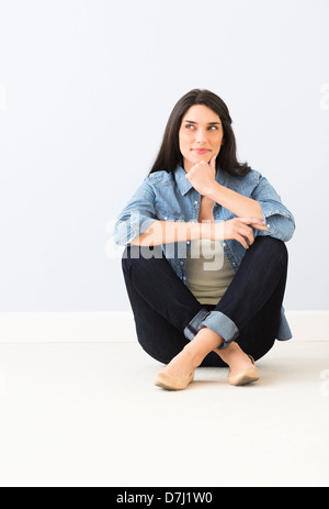 Studio portrait of young woman sitting on floor Banque D'Images