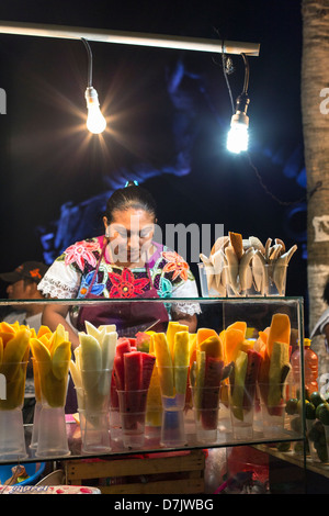 Mayan femme vendant des fruits épluchés à un stand de nourriture dans la soirée Banque D'Images