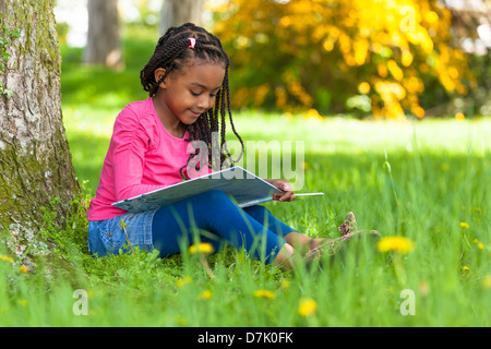 Outdoor portrait of a cute young black petite fille lisant un livre - les peuples africains Banque D'Images