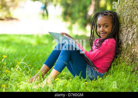 Outdoor portrait of a cute young black petite fille lisant un livre - les peuples africains Banque D'Images