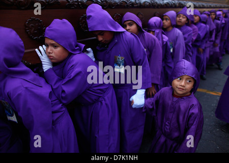 Un petit enfant, tenir la main d'un garçon qu'il transporte un trône au cours de la Semaine Sainte à La Antigua Guatemala Banque D'Images