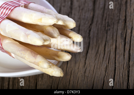 Offre groupée de l'asperge blanche avec tissu vichy rouge et blanc ruban dans un plat en porcelaine sur planche de bois rustique Banque D'Images