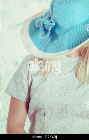 Une fille blonde se cache sous un immense chapeau turquoise Banque D'Images