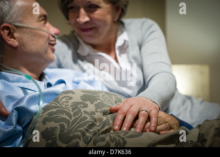 Vieux couple holding hands homme malade au lit Banque D'Images