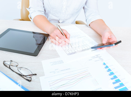 La businesswoman sitting at desk in vêtements décontractés et à l'aide de dispositifs modernes d'analyse des statistiques de ventes Banque D'Images