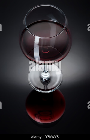 Un verre rempli de vin sur une surface réfléchissante noire Banque D'Images