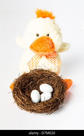 Un jouet en peluche canard et un nid plein d'oeufs de bonbons. Concept de Pâques. Isolé sur blanc. Banque D'Images