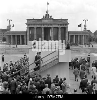 Président américain John F. Kennedy visite un view point au mur de Berlin le 26 juin 1963. Les fonctionnaires de la RDA avait couvert la porte de Brandebourg avec un drapeau rouge et a également installé une affiche traitant directement de la présidente. Banque D'Images