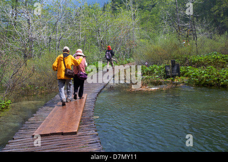 Touristes marchant le long d'un chemin de promenade en bois à travers les lacs du parc national des lacs de Plitvice, un site du patrimoine mondial de l'UNESCO, en Croatie en mai Banque D'Images