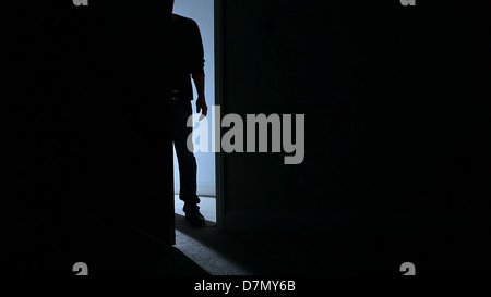 Silhouette d'un homme debout dans une porte menant à une pièce sombre. Banque D'Images