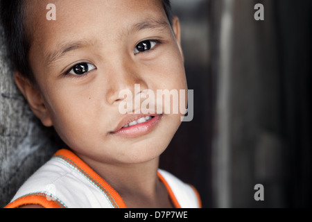 Jeune garçon asiatique avec sourire doux qui vivent dans la pauvreté région sinistrée - portrait contre mur. Manille, Philippines. Banque D'Images